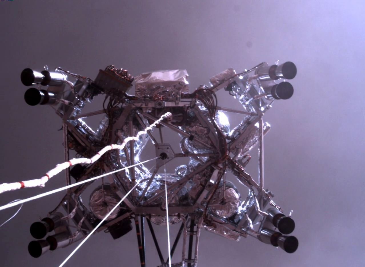 La "skycrane" photographiée par Perseverance juste avant qu'il se pose sur Mars, suspendu aux cables. Les moteurs sont allumés mais ne produisent pas d'effet visuel. Crédits NASA/JPL-Caltech