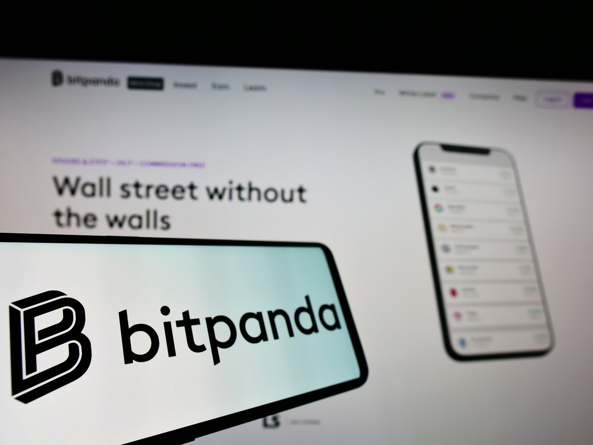 Le logo de Bitpanda apparaît sur un smartphone, devant un écran affichant l'interface de la plateforme crypto © Shutterstock