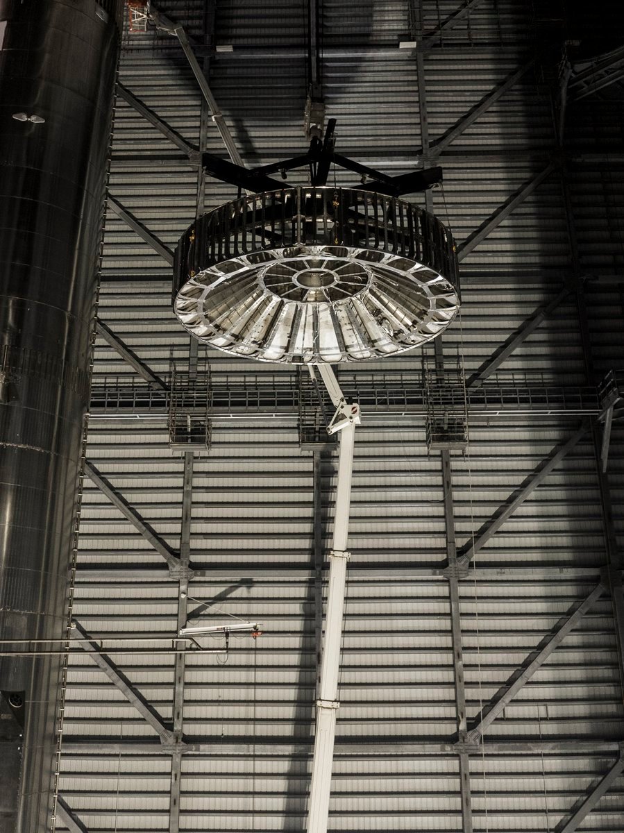 La nouvelle pièce d'interétage en cours d'assemblage. Les grilles permettront aux moteurs de Starship de s'allumer avant la séparation de l'étage, tandis que le dome blindé protège SuperHeavy juste dessous © SpaceX