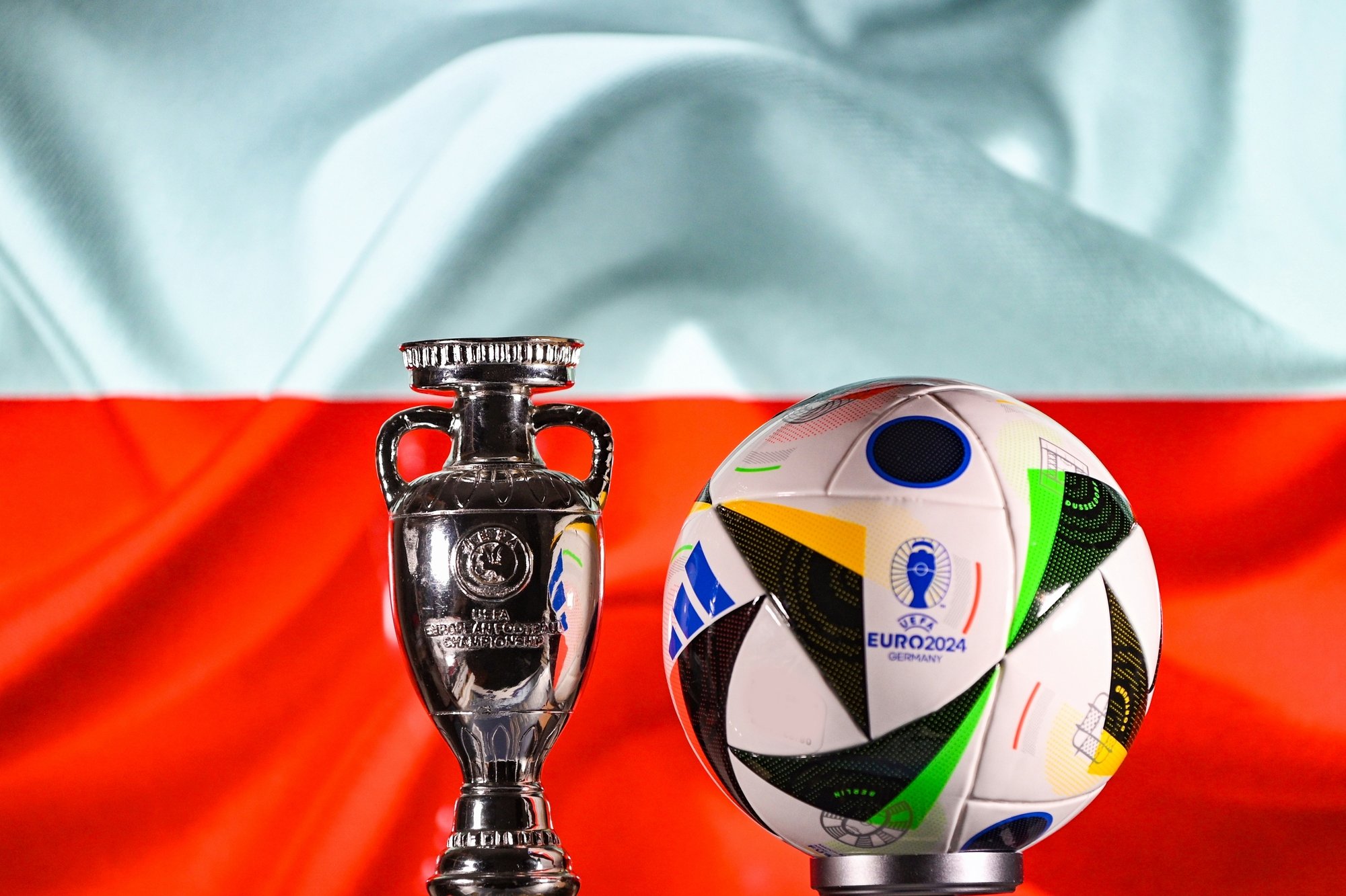 Le ballon officiel et la coupe de l'Euro 2024, avec le drapeau polonais en fond © fifg / Shutterstock