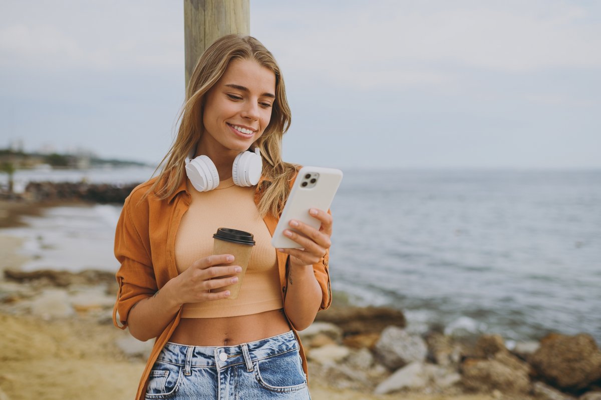 Une jeune femme smartphone en main, profitant du bord de mer © ViDI Studio / Shutterstock