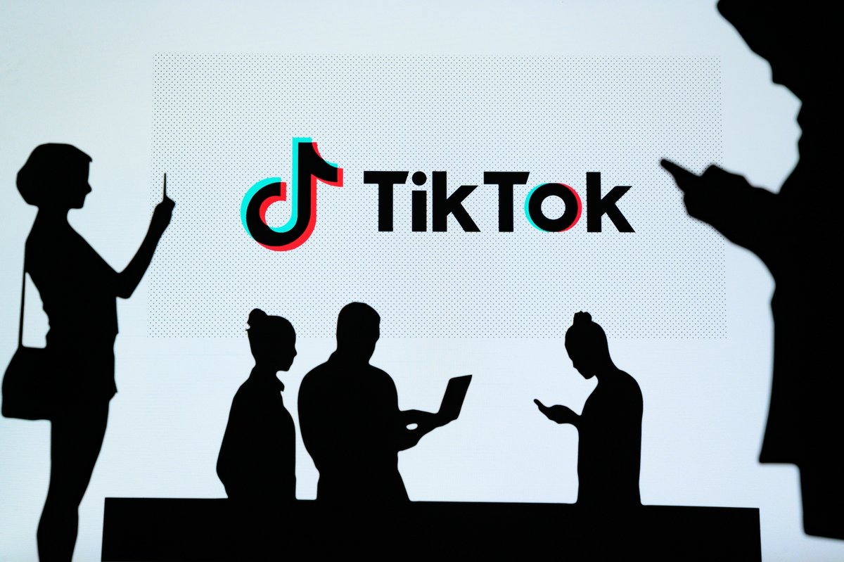L'ombre de personnes utilisant leur smartphone, avec au milieu le logo de TikTok © kovop / Shutterstrock