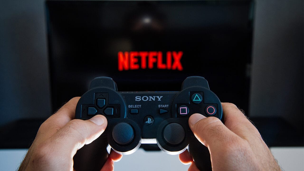 Une manette de console de jeu vidéo tenue devant un écran Netflix © Getty Images