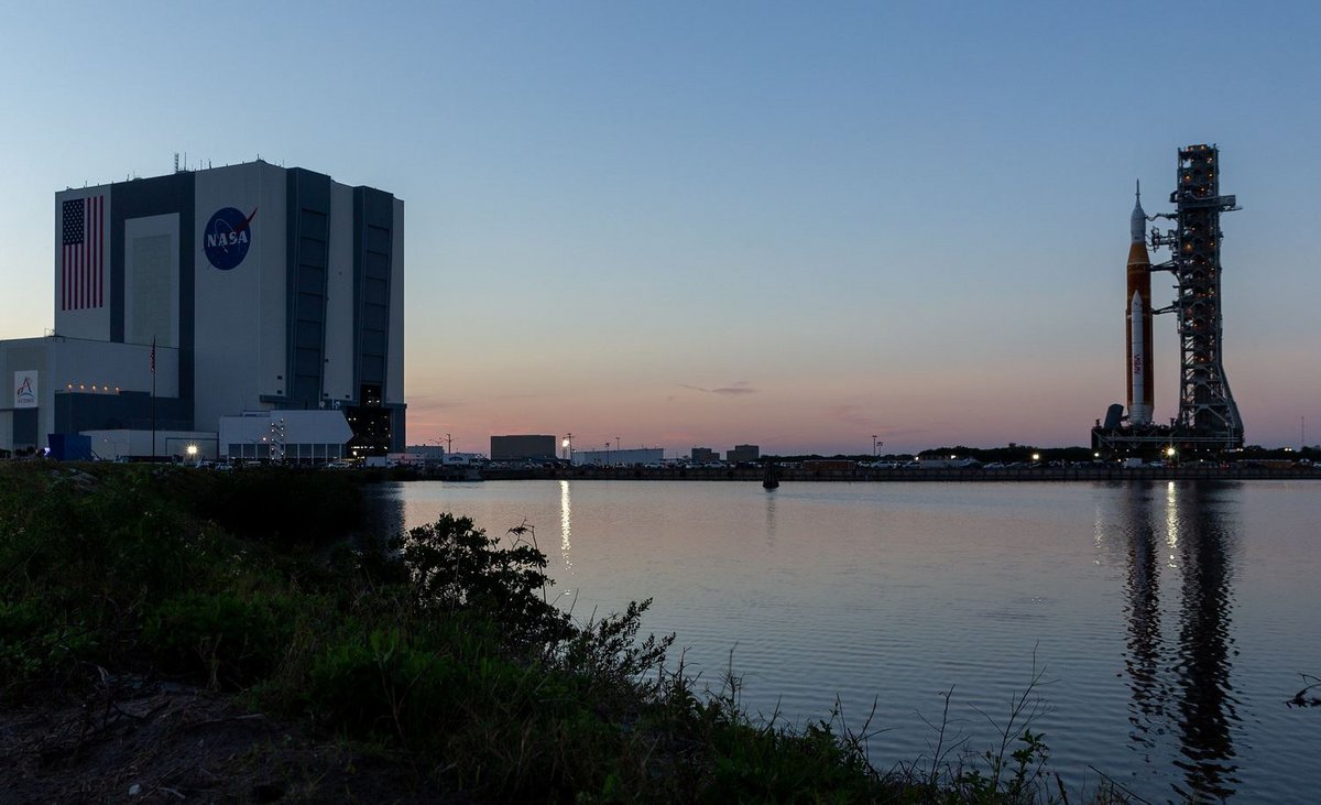 Le bâtiment d'assemblage (VAB) à gauche laisse partir le lanceur SLS vers son site de lancement. Il y reviendra dans quelques semaines après ses tests. Crédits : NASA