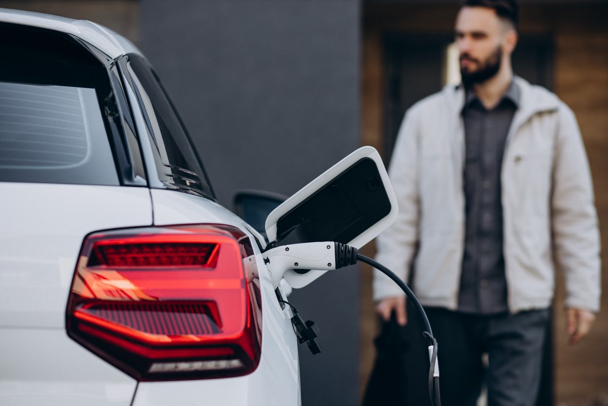 Un homme face à une voiture électrique en cours de rechargement © PH888 / Shutterstock