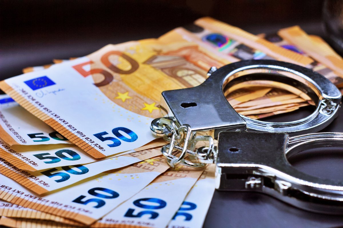Une paire de menottes de police sur des billets en euros © RaffMaster / Shutterstock